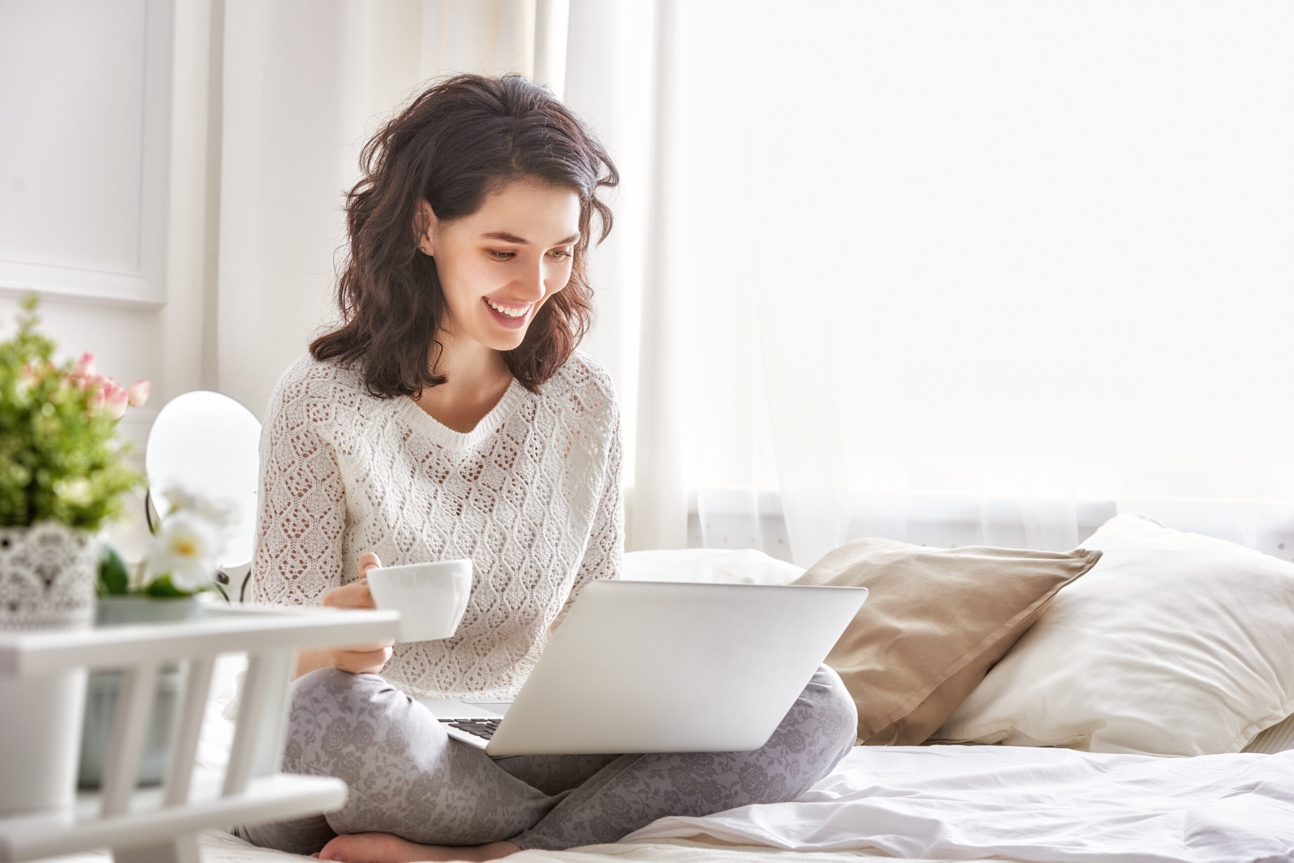 smiling woman holding a cup in front of a laptop